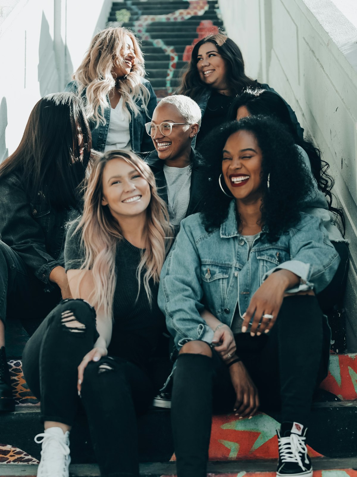 A diverse group of women laughing together on colorful outdoor stairs.