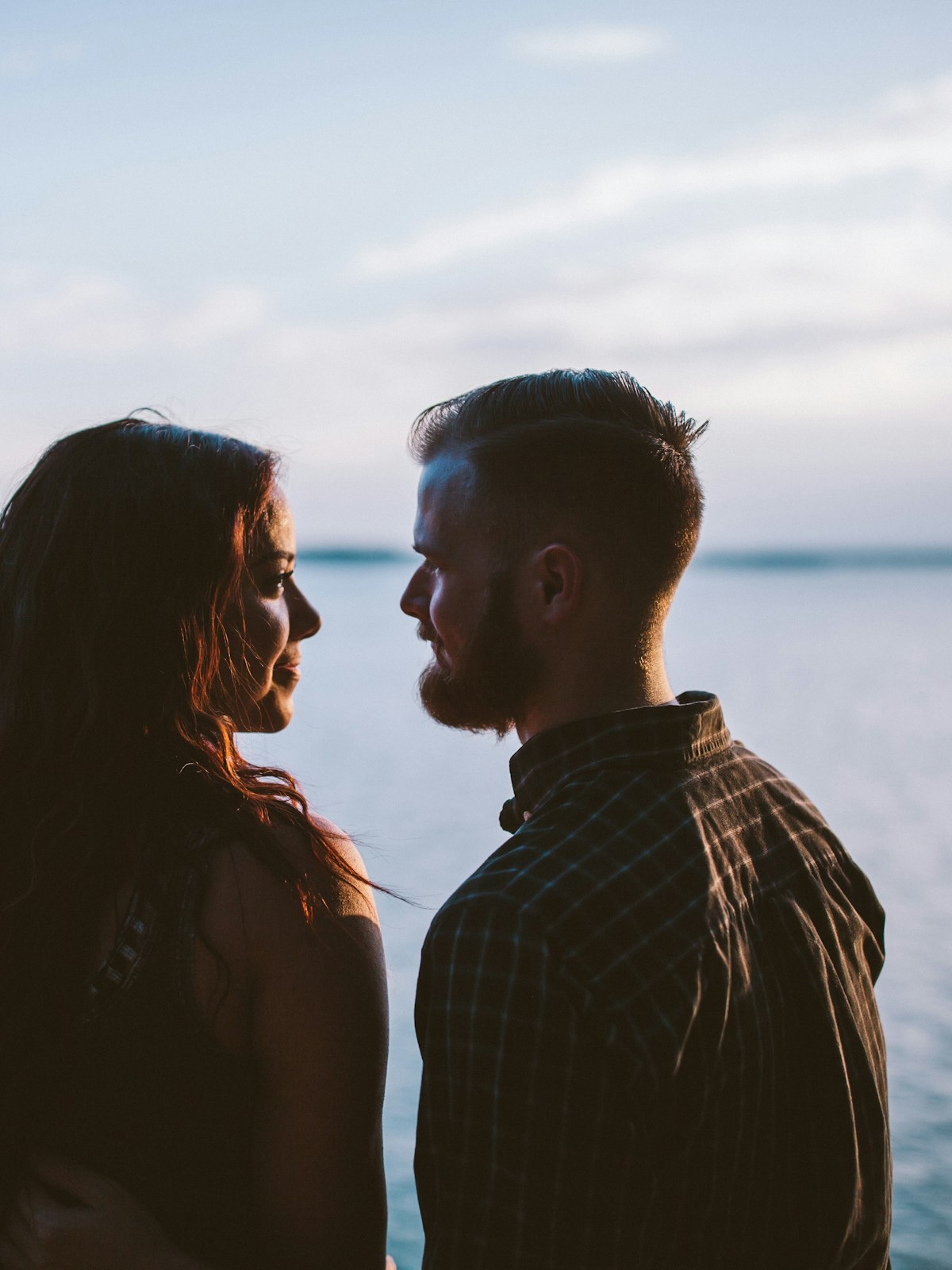 Two people close to each other at golden hour, gazing toward one another over water.